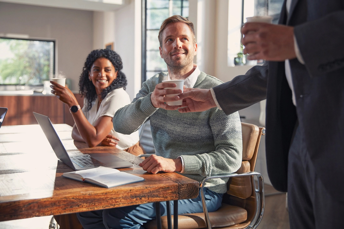 Drie personen in een modern kantoor discussiëren rond een tafel met laptops.